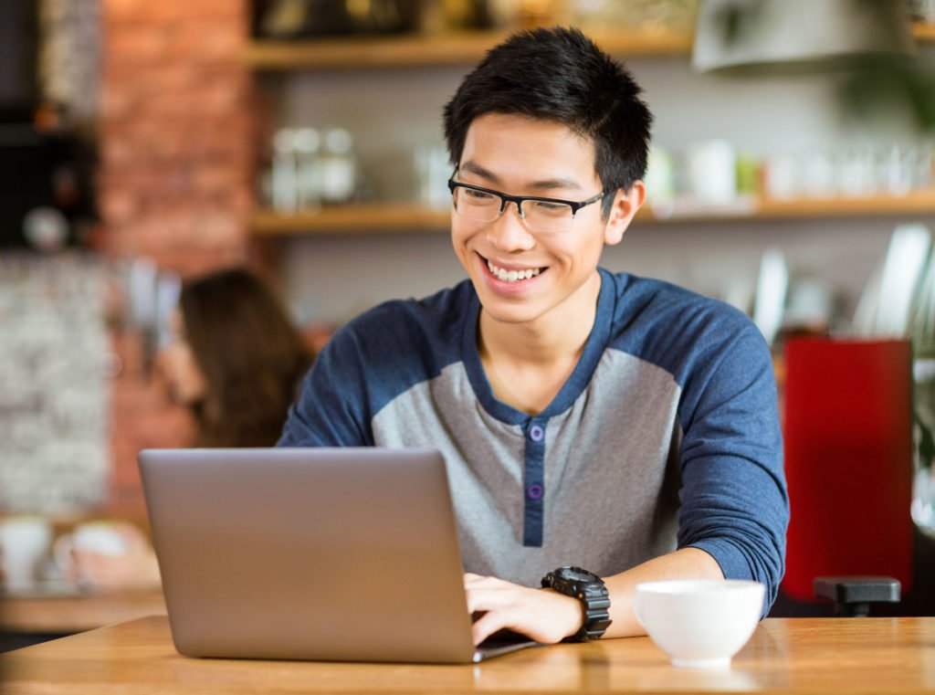 young asian man at a cafe looking at his laptop