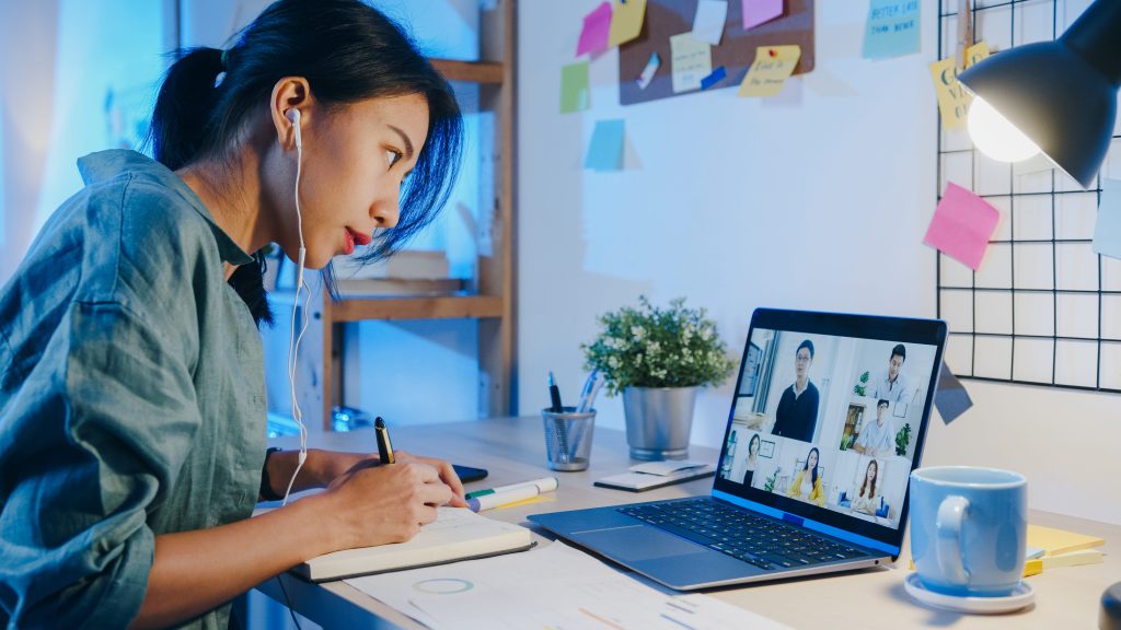 Female student attending a virtual class on a laptop while writing in a notebook