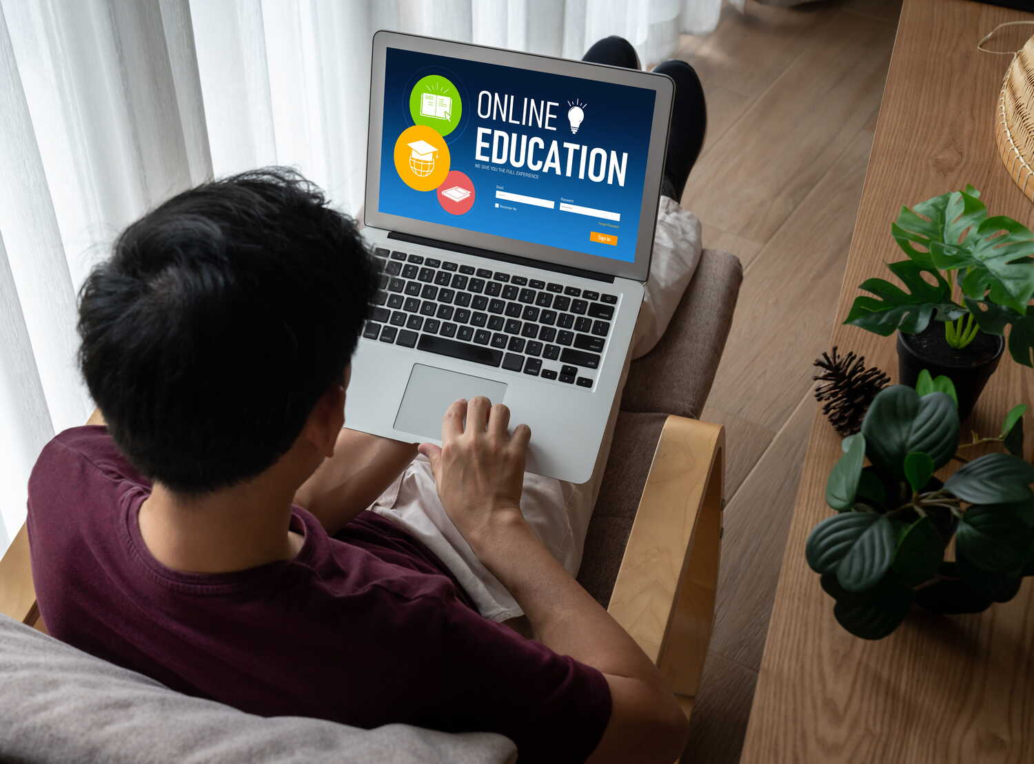 A male student browsing an online education website on a laptop while relaxing on a couch at home.