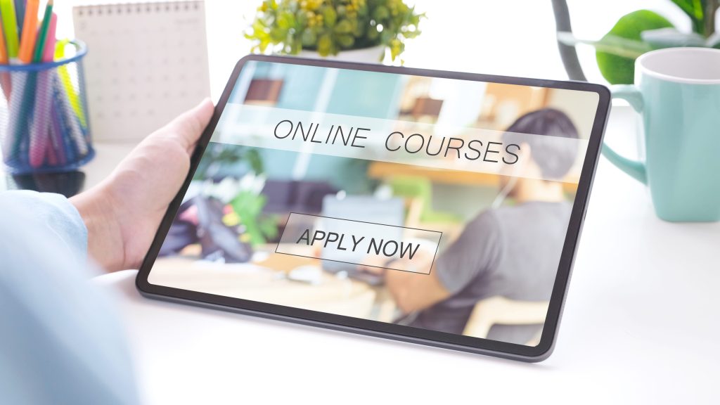 Hand holding a tablet displaying an online course enrollment page with an Apply Now button