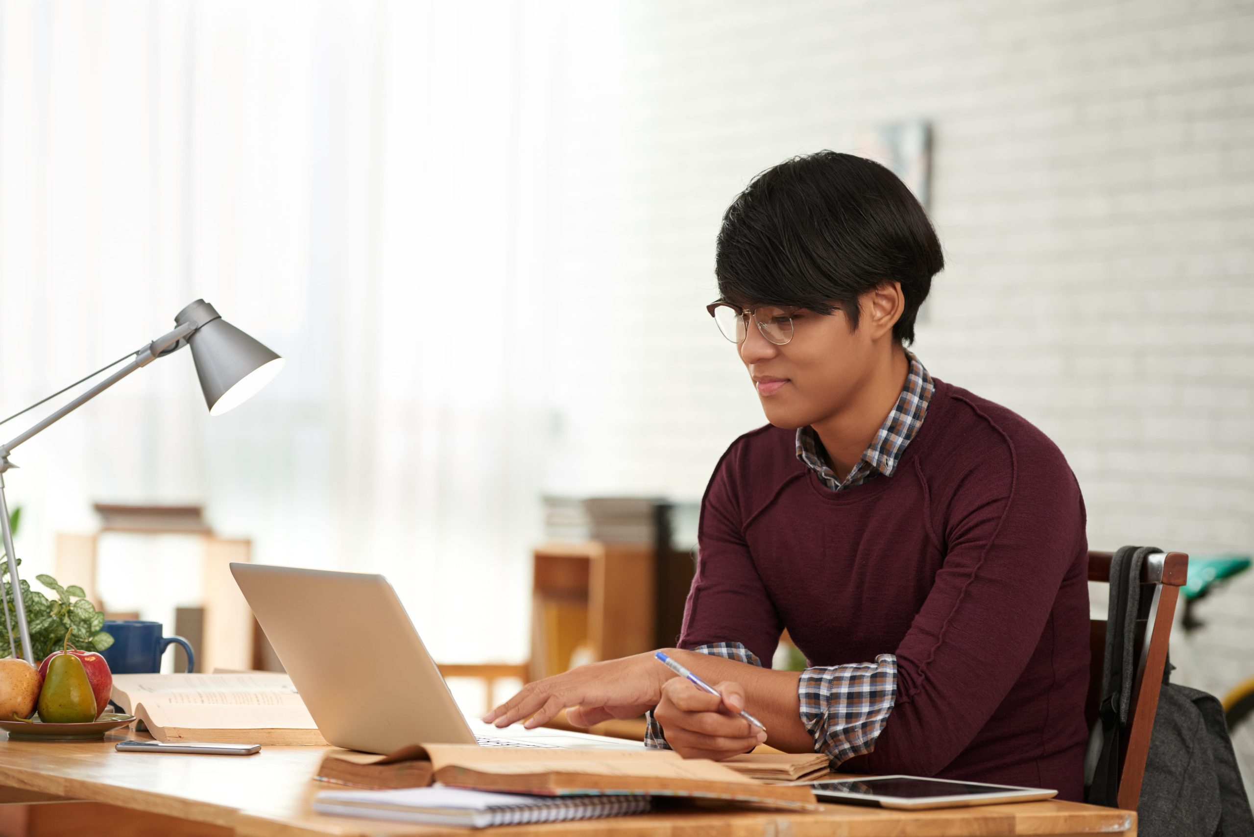 Young man leaning toward a laptop screen while studying at a home desk