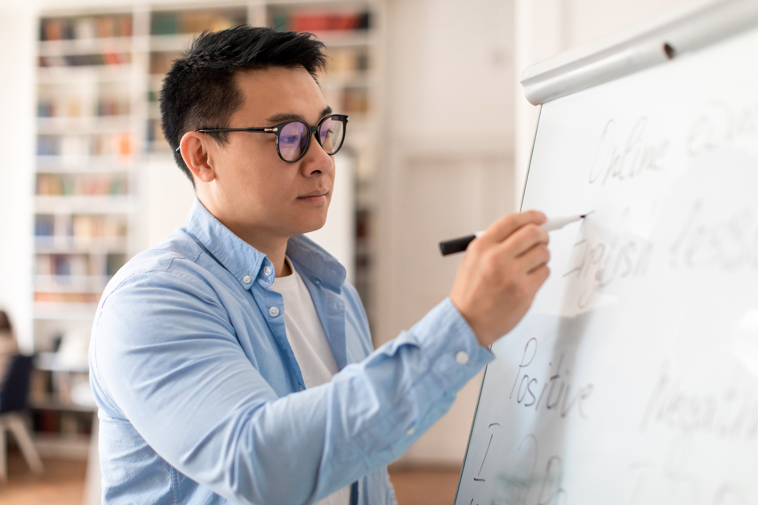 A professor wearing glasses writes grammar rules on a whiteboard in a classroom setting